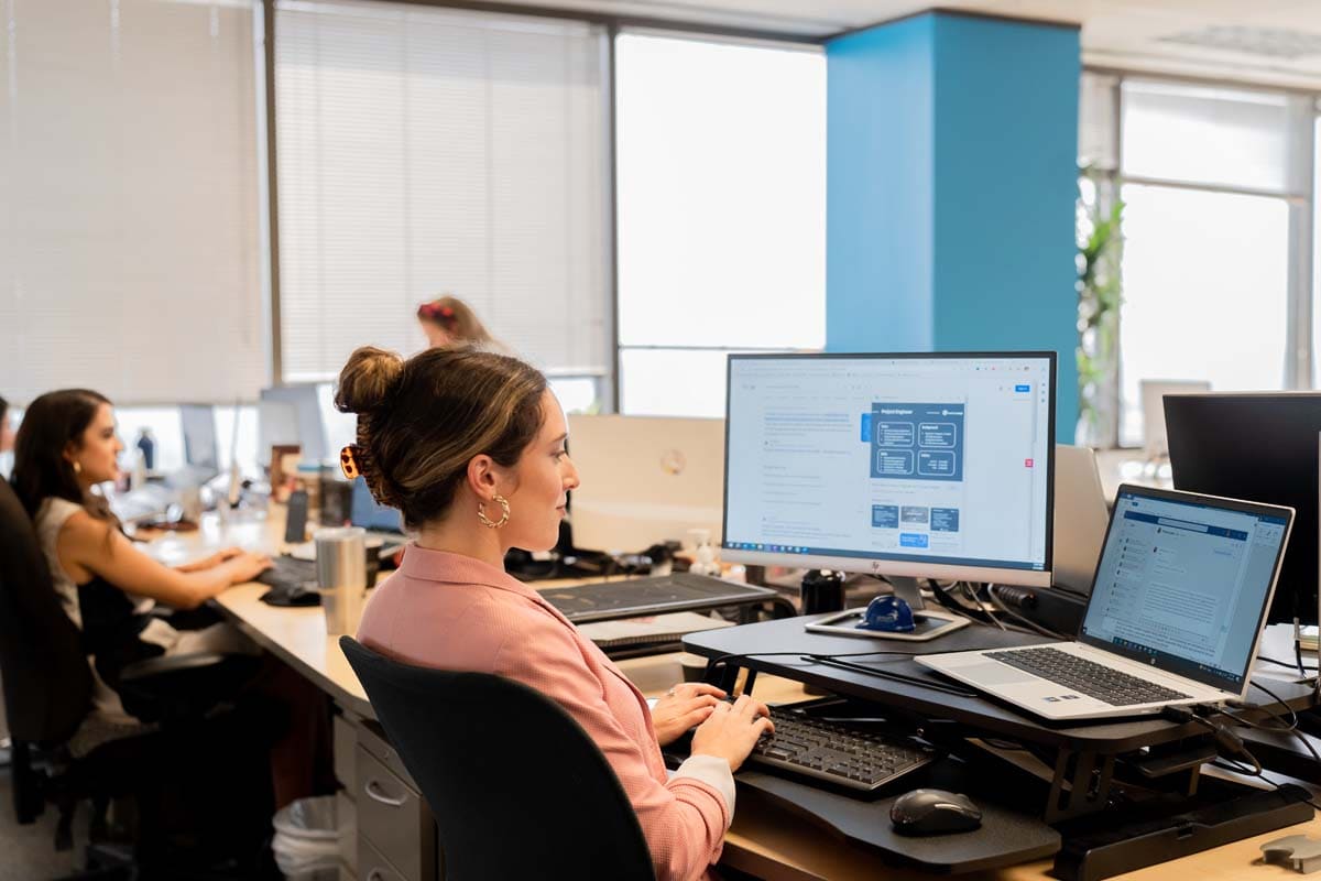 Lady in working at her desk in an office with her laptop open and computer screen